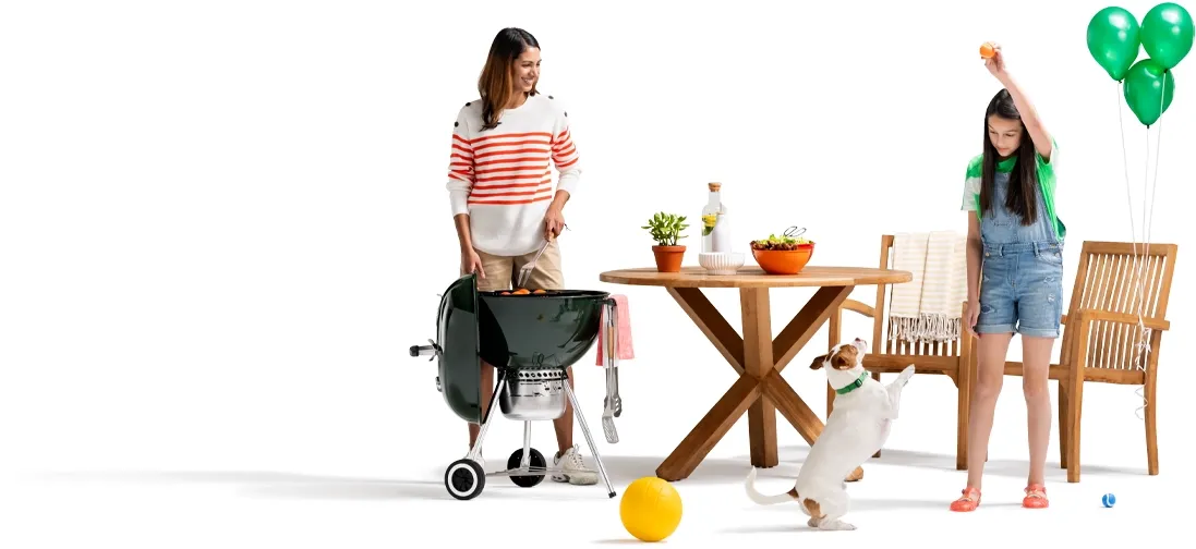 As mom tends the grill next to the outdoor patio furniture, her daughter plays fetch 与 their Jack Russell terrier A trio of green balloons are tied to the wooden picnic chair.